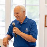Jim Scott standing at podium with microphone, smiling at someone in crowd